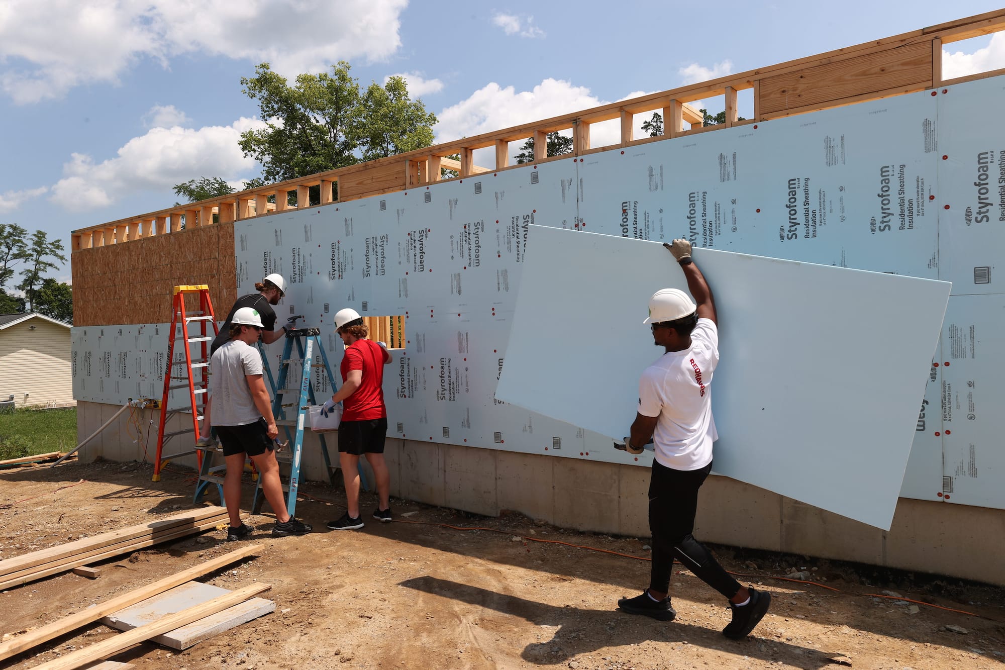 Several students nail foam insulation sheets to a plywood wall