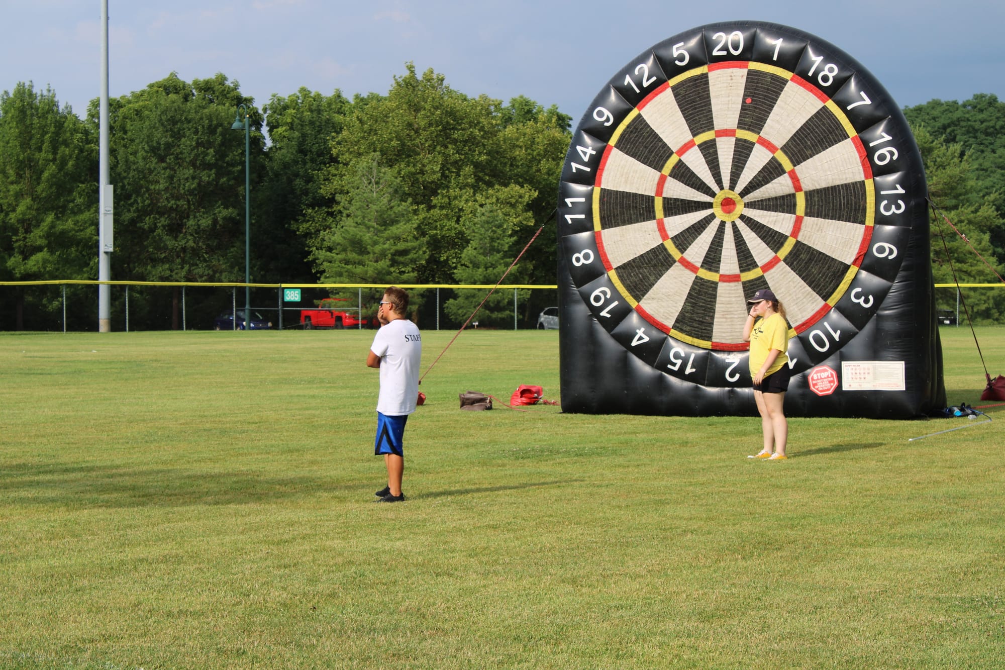 Two staff members stand in front of a 20-foot tall velcro dart board