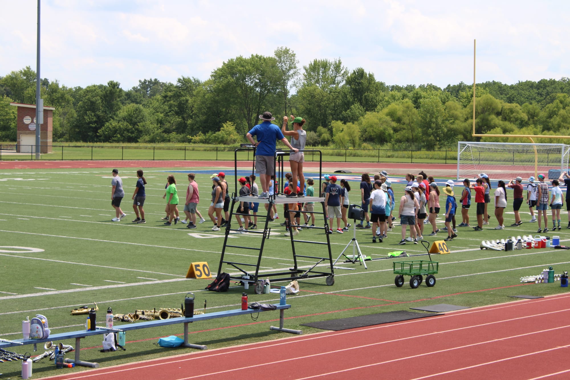 Students stand in formation on a football field, with Sadie Abbitt and Mike Marston on a raised platform