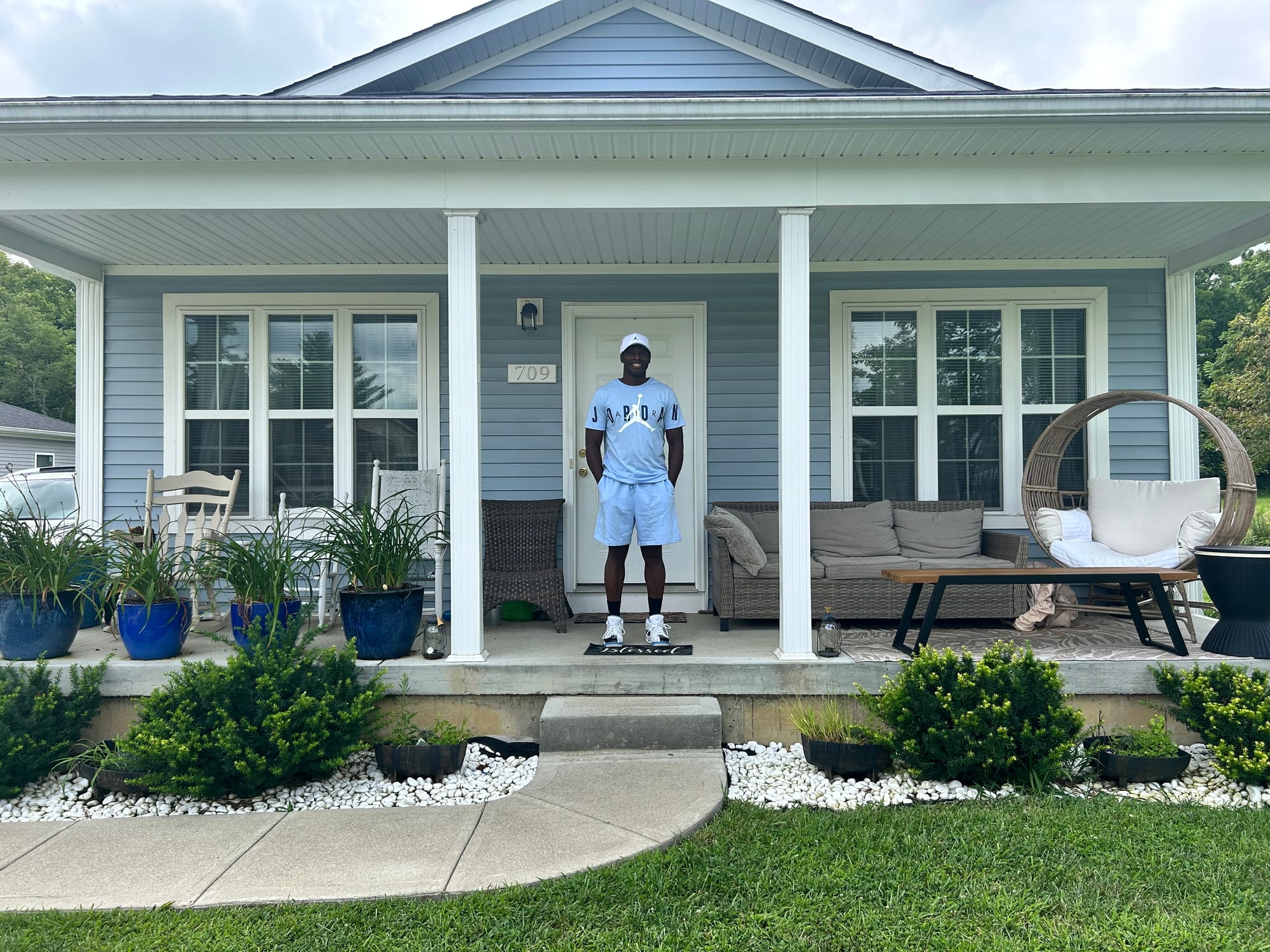 A man in a blue shirt and shorts stands on his porch