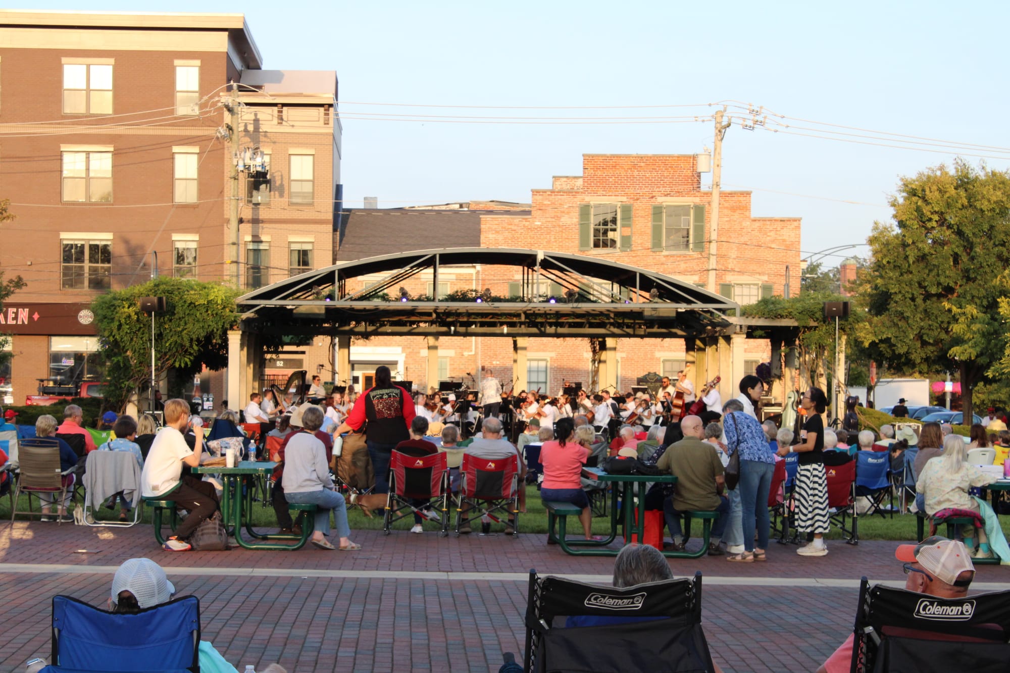 A crowd sits in the park in lawn chairs