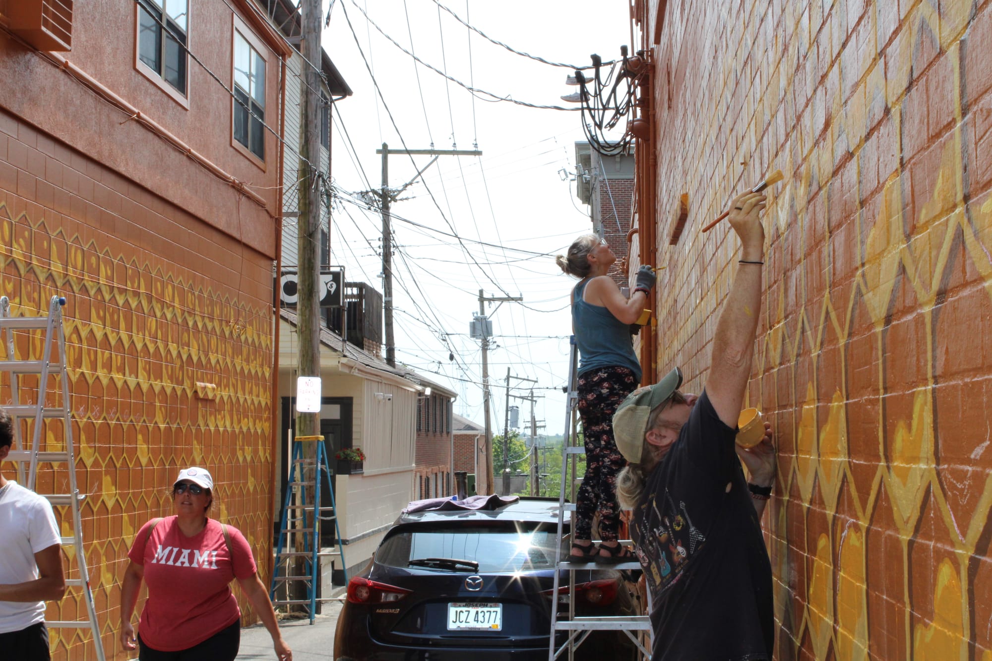 Joe Prescher stretches to paint a honeycomb cell on the mural