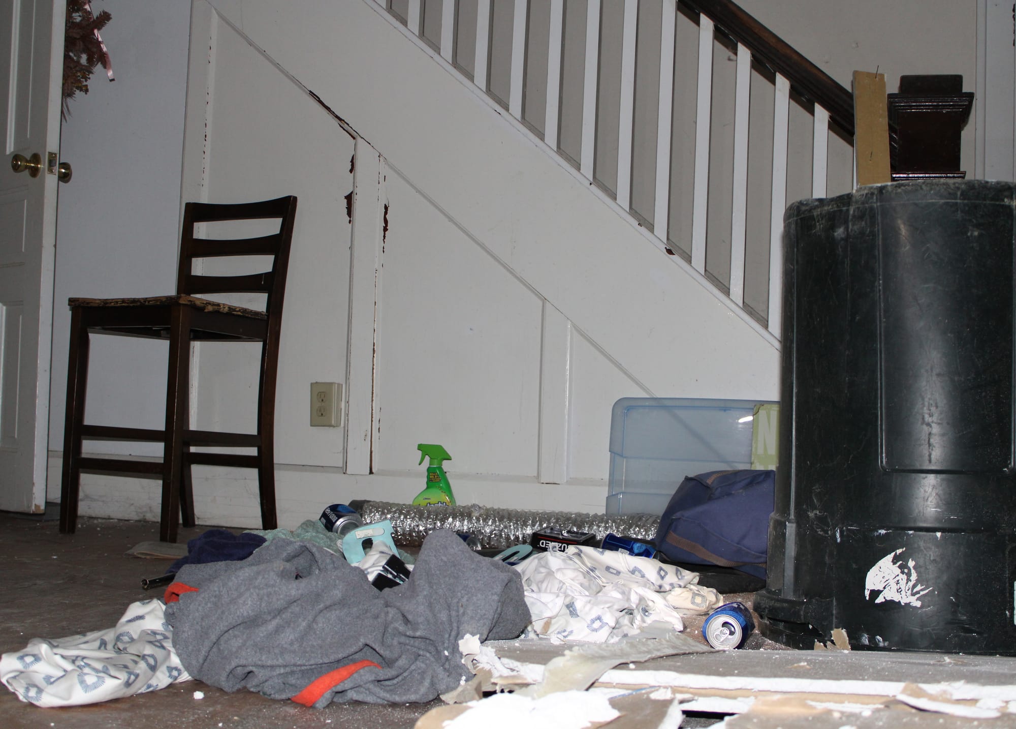 Trash and old clothing litter the floor in front of a staircase