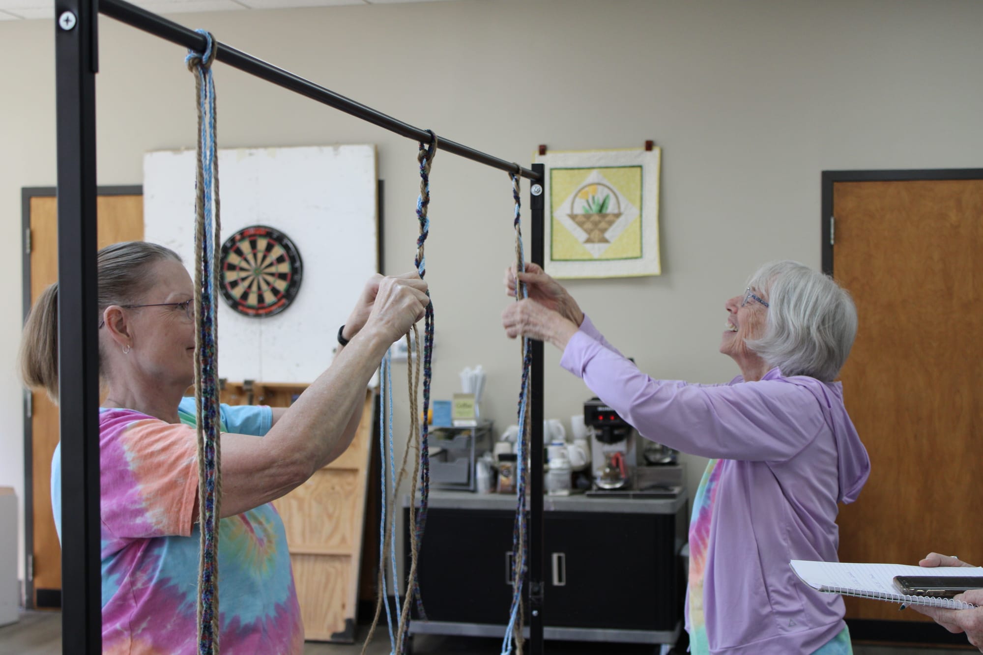 Jessica Kopp and another woman stand on either side of a metal coat rack with ropes hanging from it