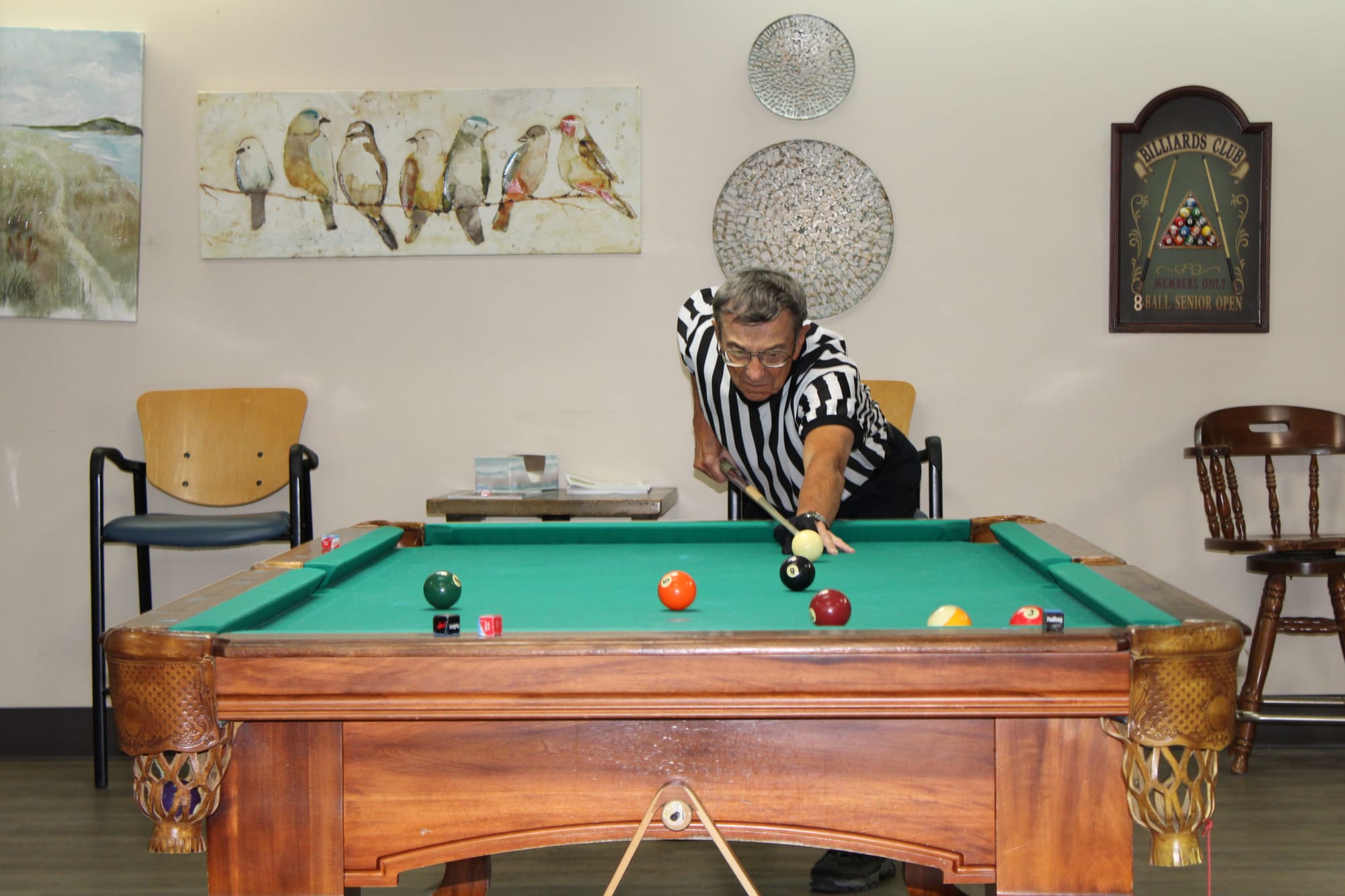 Ron Zemko lines up a shot on the opposite side of a pool table while wearing a striped ref shirt