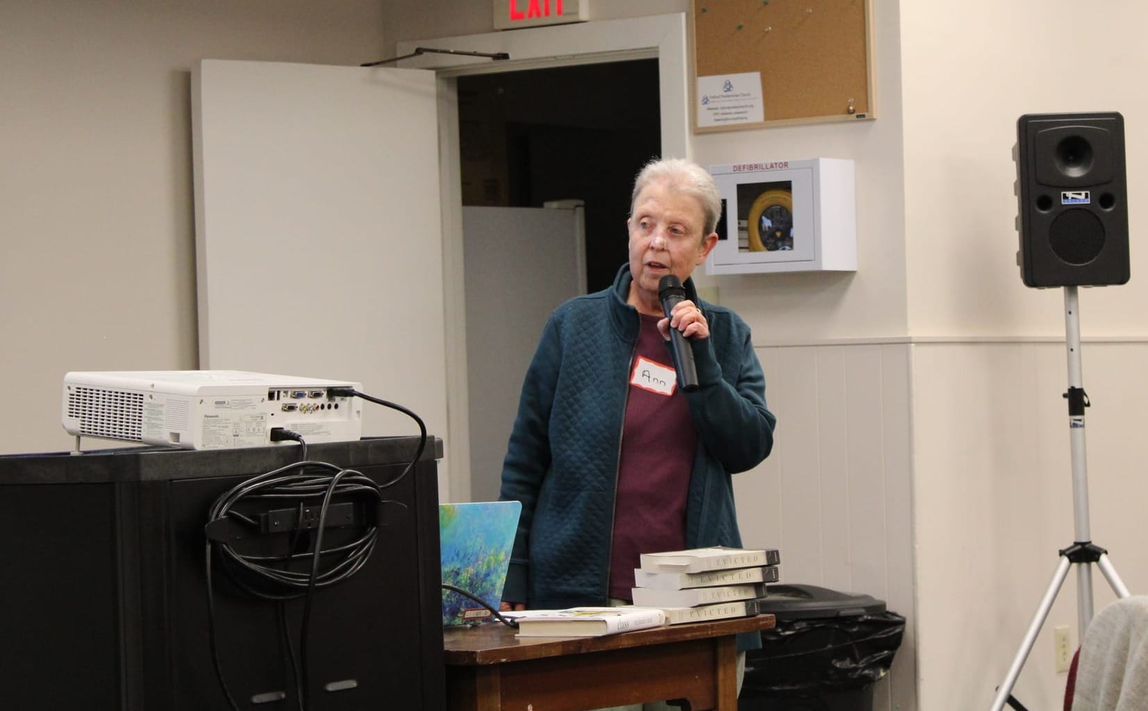 Ann Fuehrer holds a microphone and speaks next to a projector