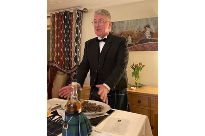 Kenneth Douglas stands at the head of a table in a kilt