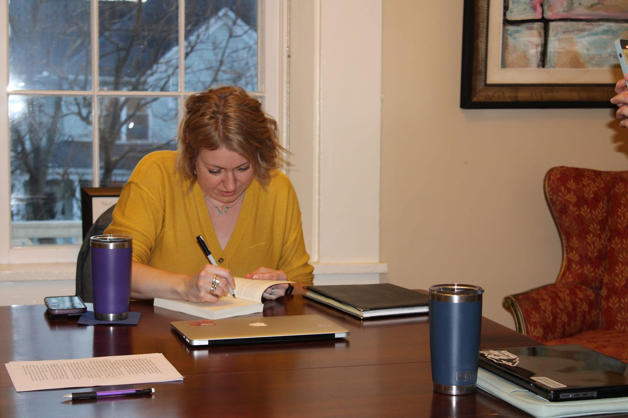 Laura Gaddis sits at the end of a table and signs a book