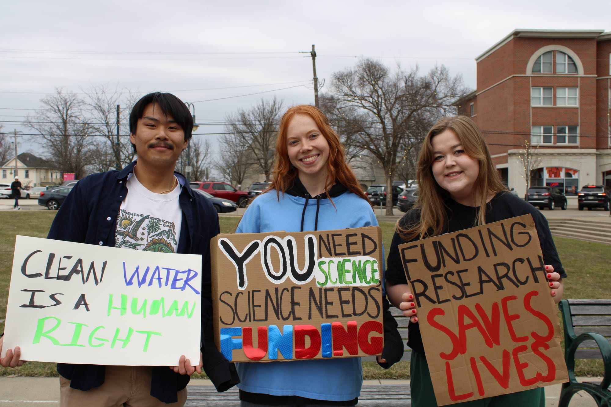 Three college students hold signs about science, including "funding research saves lives"