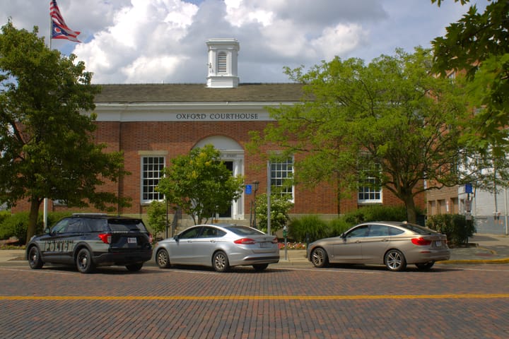 A red brick building with a sign reading "Oxford Courthouse" sits across a brick street during the day.