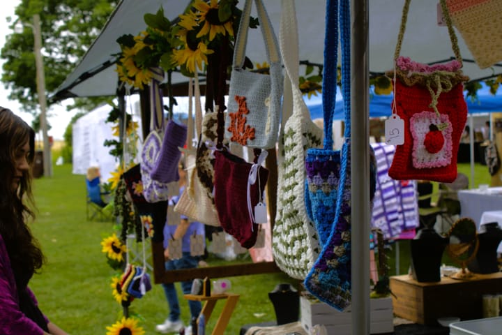 A brunette woman organizes her table underneath an array of hanging hand-crocheted bags.