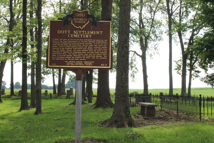 A wooded cemetery with an Ohio Historical Marker that reads "Doty Settlement Cemetery"