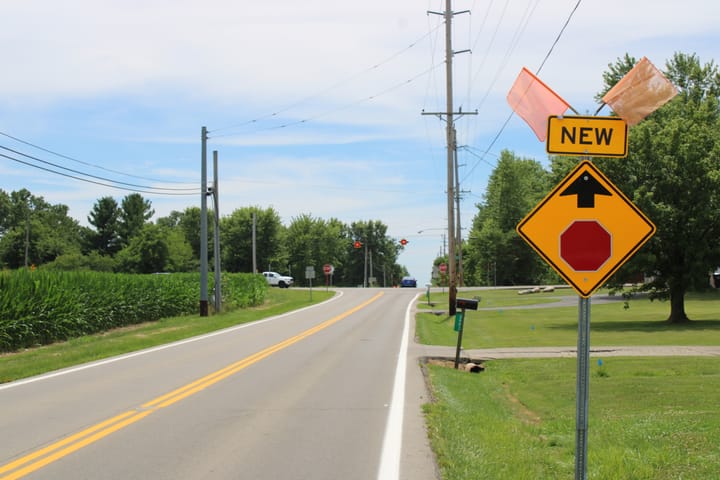 road with a yellow sign showing a stop sign ahead, and a sign that reads "new" above it