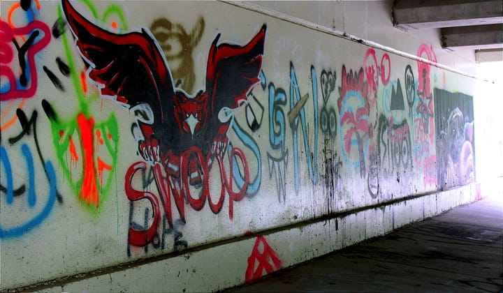 Graffiti covers a white wall under a road. The images include a Miami RedHawk and baby yoda