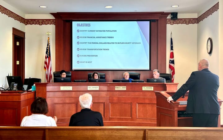 4 Commissioners sit behind their curved wooden desk, adorned with name plaques, and discuss the agenda for the day.