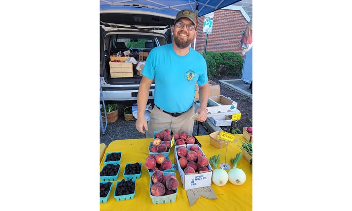 Larry Johnson stands behind a table with peaches, blackberries and other goods on it