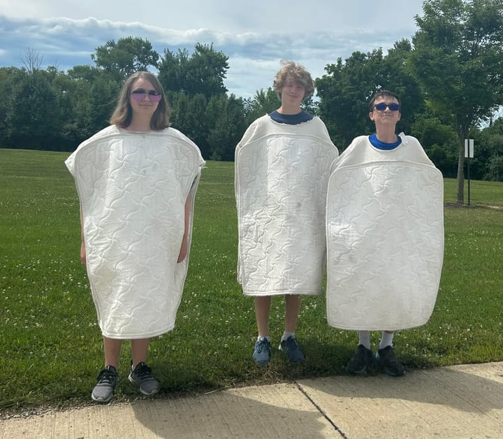 Three students stand in grass wearing mattress costumes