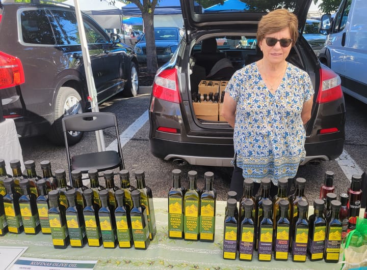 Evie Semertzides stands behind a table with dozens of olive oil bottles on it