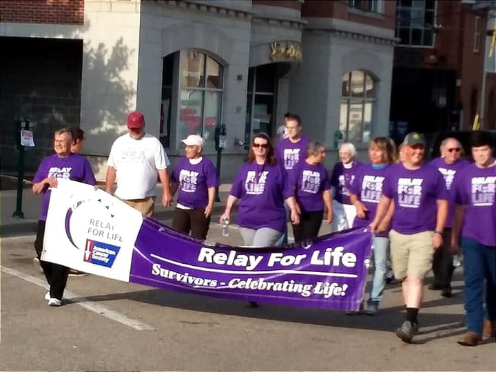 About 15 people in purple shirts walk in Relay for Life event.