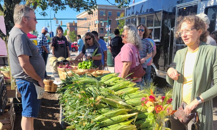 Several people stand near a table piled high with corn