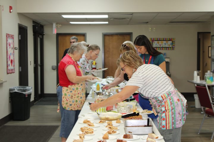 Several older adults get food at a long buffet table