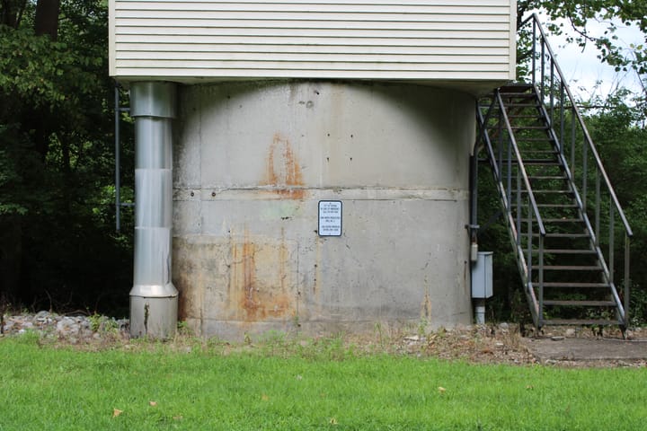 A concrete water production well with metal stairs on the right and a wide metal pipe on the left