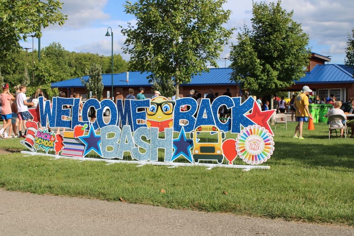 Dozens of people line up behind a large "Welcome Back Bash" yard sign