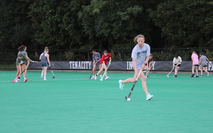 Ellery Duval runs on a field with a field hockey stick