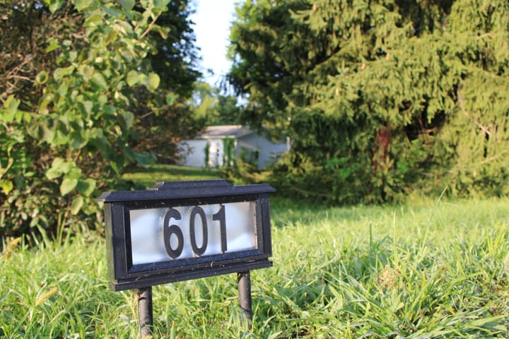 A sign labeled "601" stands in the grass in front of trees and a house