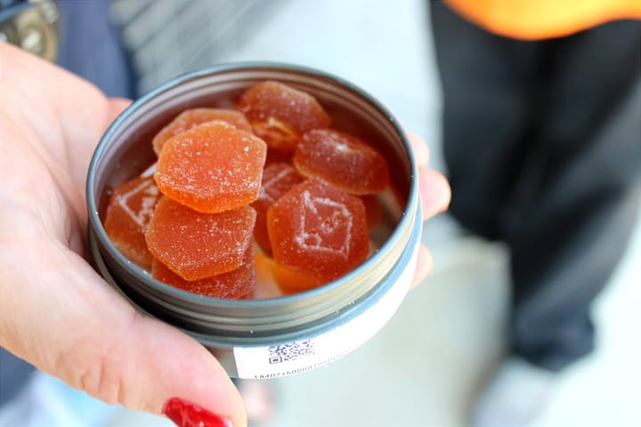 A woman holds orange edibles in a circular metal container