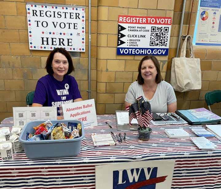 Two volunteers sit behind a table with signs about registering to vote