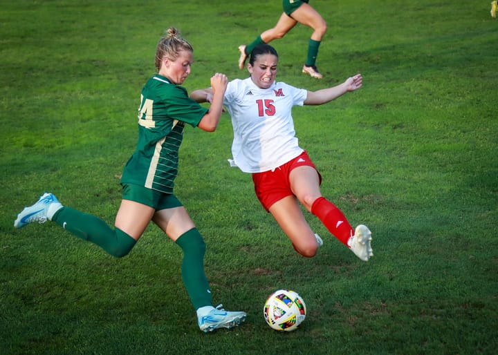 Two soccer players on different teams attempt to kick the ball