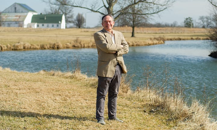 Tom Cooke stands in a field next to a lake