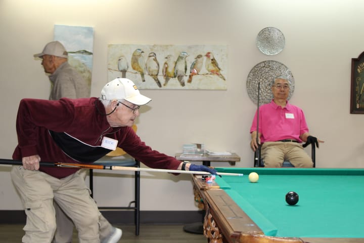 Nick Asher stands to the left of a pool table and lines up his cue