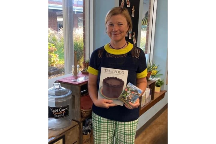 Kate Currie holds up a cookbook titled "True Food"