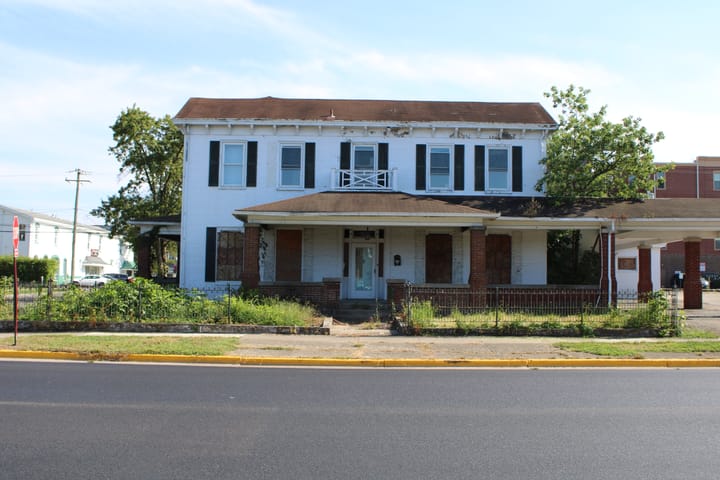 101 W. Church Street seen from the front, with tall gras and boarded up windows on the first floor