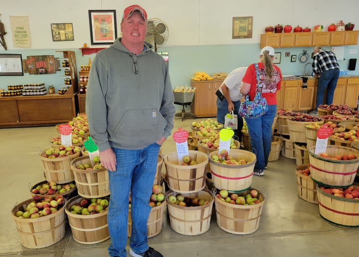 Scott Downing stands in front of dozens of baskets full of apples