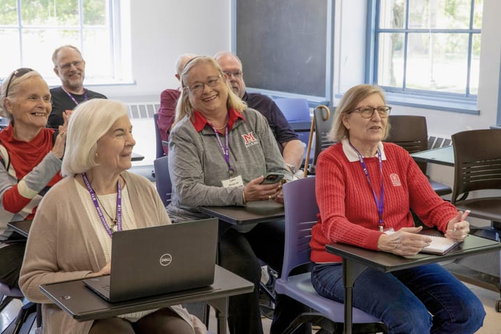 Several older adults sit in a classroom smiling