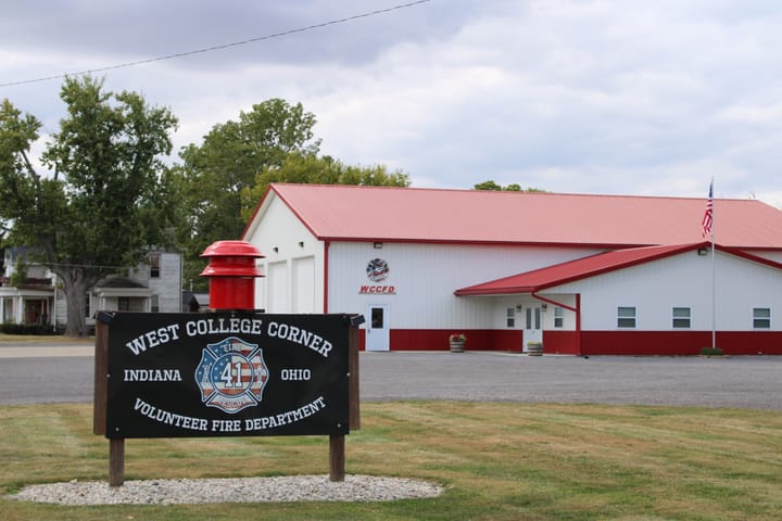 The West College Corner Volunteer Fire Department building has a sign and a red roof