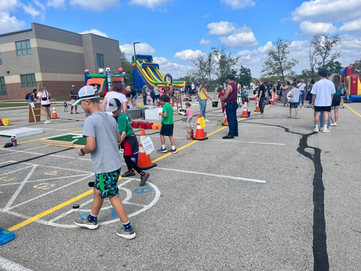 Children play games in a parking lot with bounce houses and other activities set up