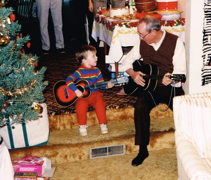 Richard Campbell's father and son sit next to each other on the floor with guitars