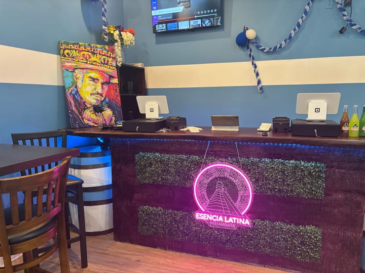 A view of the front counter at the restaurant featuring a pink light-up Esencia Latina sign