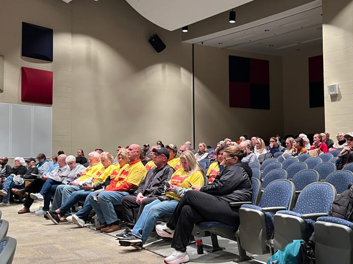 An audience in an auditorium, including several people in matching yellow shirts with red Ohio maps