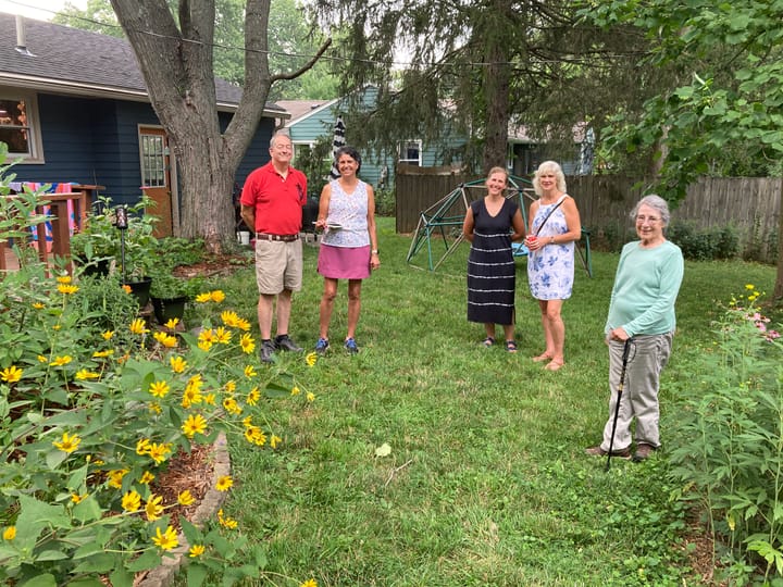 Several people stand in a grass lawn with flowers and other plants