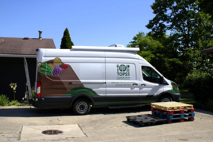 A white van with a graphic of a bag full of food and the TOPSS logo