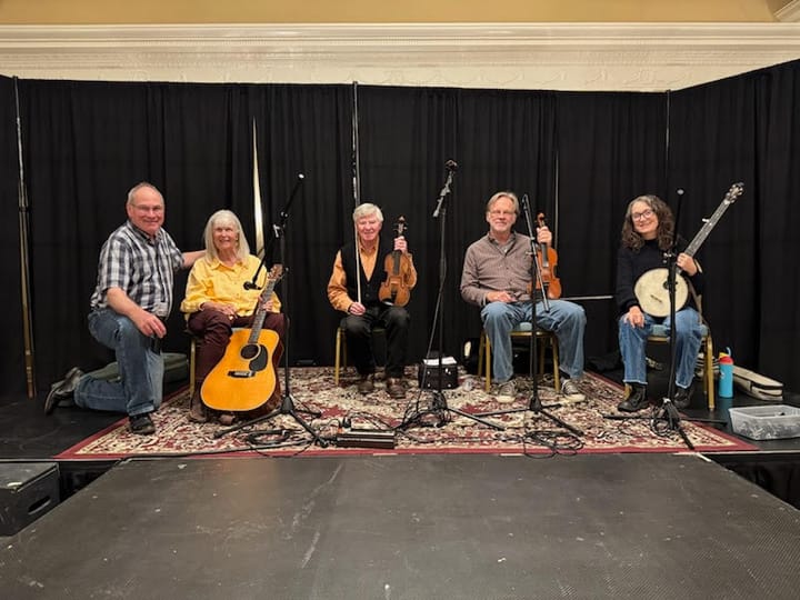 Five musicians sit on stage in front of a black curtain