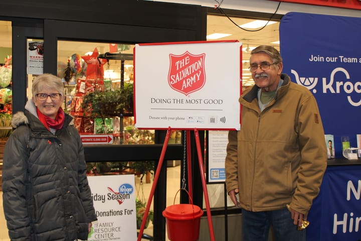 Bobbe Burke and Bob Carmean stand on either side of a Salvation Army donation bucket