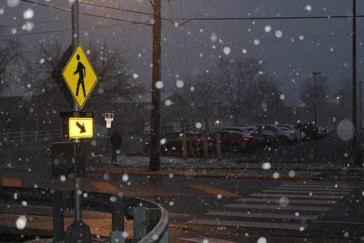 A crosswalk sign on S. Locust Street at dusk in the snow