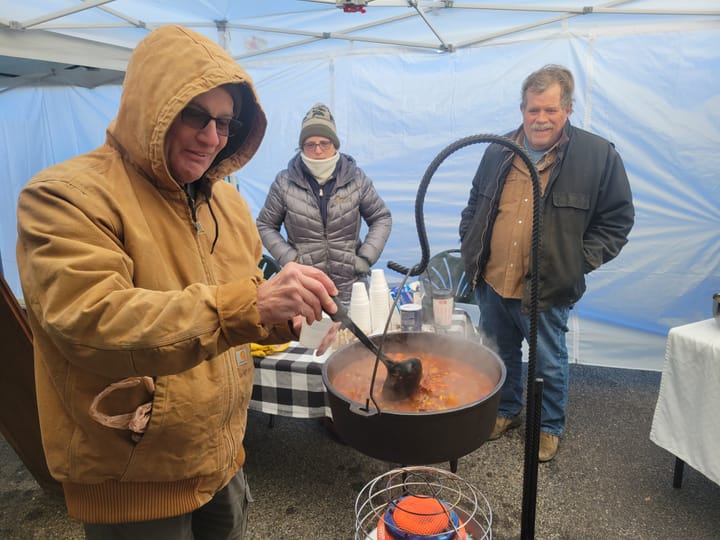 Larry Slocum dips a ladle into stew suspended above a heater