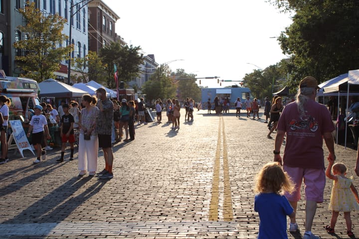 Dozens of people walk down High Street and visit booths in the sun